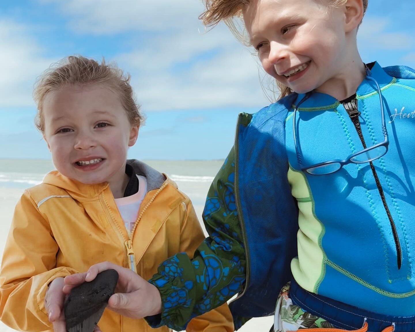 Two young kids on a Charleston beach holding a fossil shark tooth they found